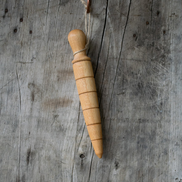 A traditional oak wooden dibber used for making neat holes in a garden bed for planting seeds to a uniform depth.