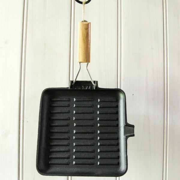 Sear meat in the kitchen or over the campfire with a pre-seasoned cast iron skillet, square 24cm x 24cm, square large 28cm x 28cm, or oblong 21cm x 35cm, with folding timber handle. 