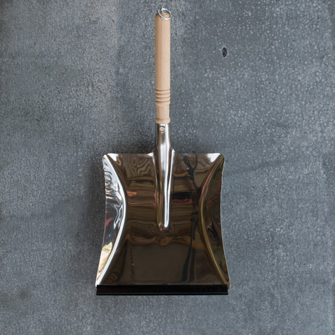 A smart stainless steel dust pan, with turned raw timber handle and metal ring at the end for hanging.