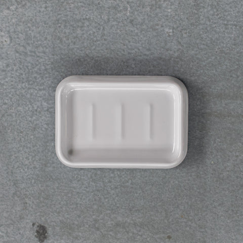 A Falcon enamel soap dish in white with blue trim on the base. The soap dish features three raised ridges so the soap drains and dries after use. 